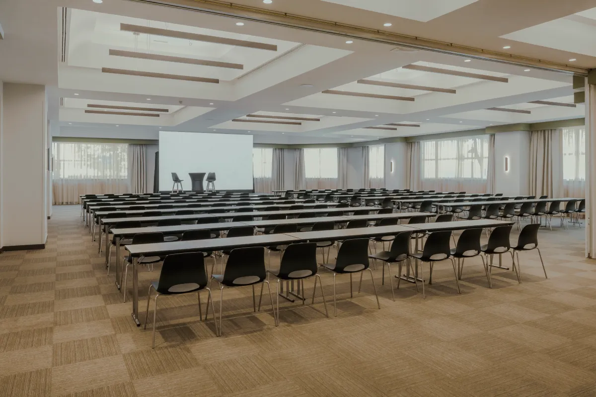 Sala de conferencias amplia con filas de sillas y proyector en el escenario