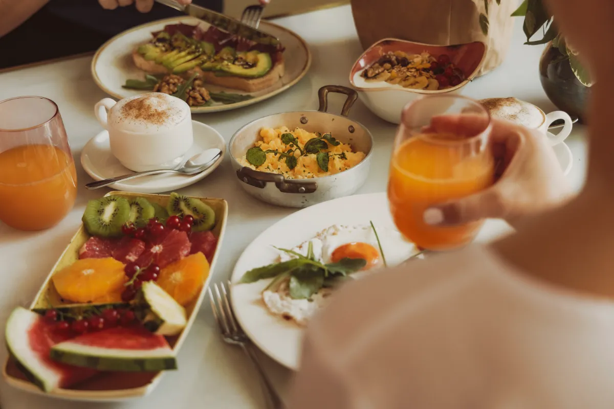 Mesa de desayuno con huevos, tostadas, frutas y jugo naranja en tazas y platos