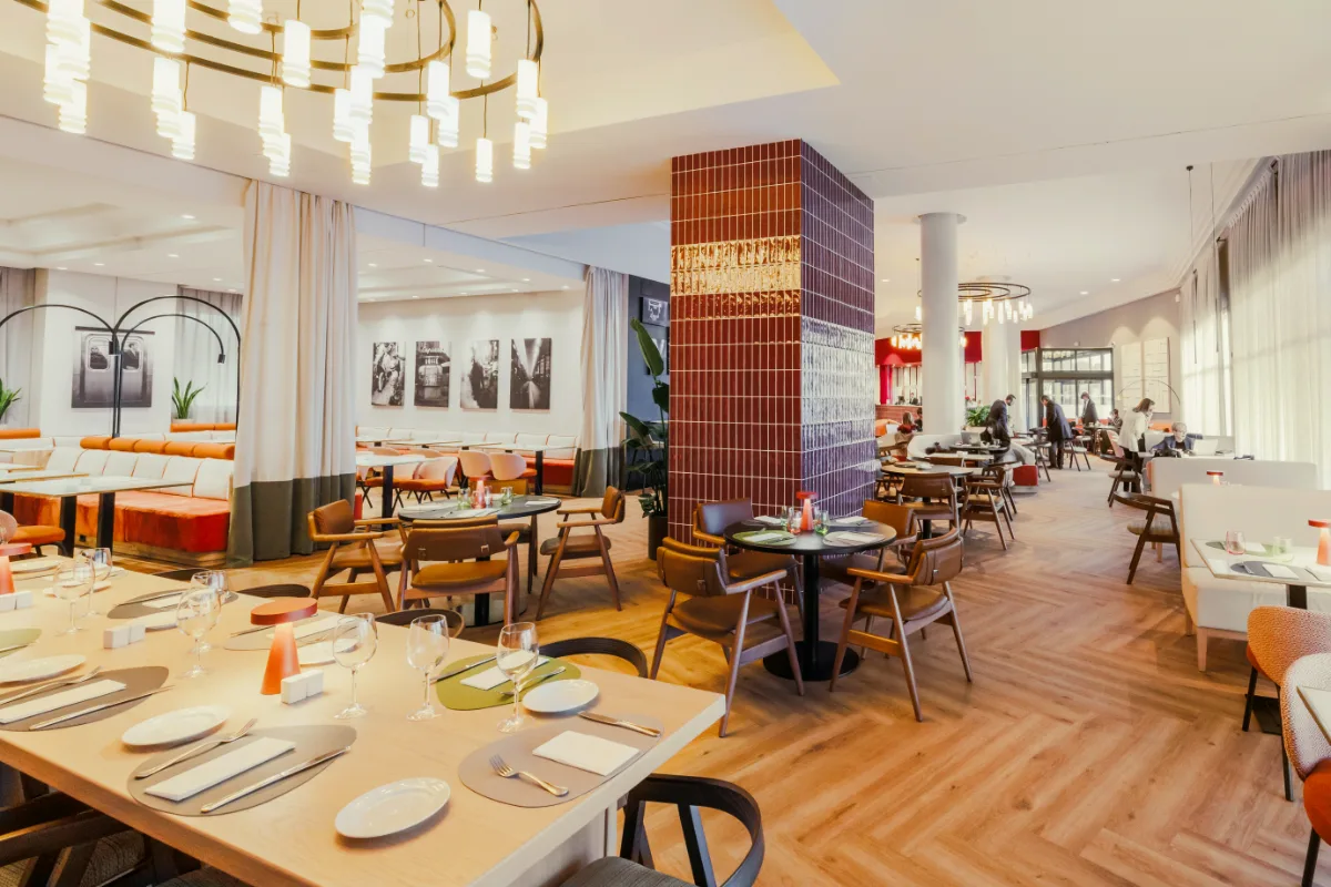 Sala de restaurante moderna con mesas y sillas, luz c&aacute;lida y barra al fondo