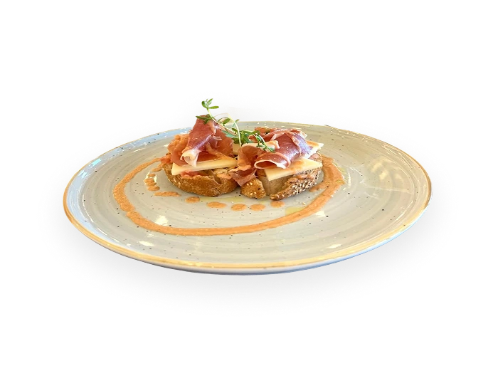 Tostada con jam&oacute;n y brotes sobre crema en plato de cer&aacute;mica blanca.