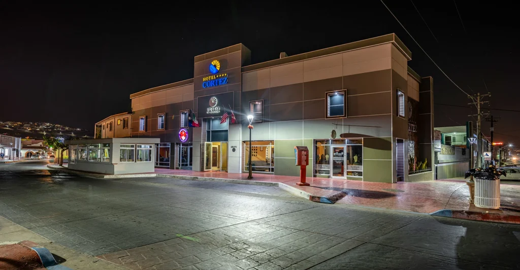Fachada iluminada del Hotel Cortez, con banderas y letrero nocturno.