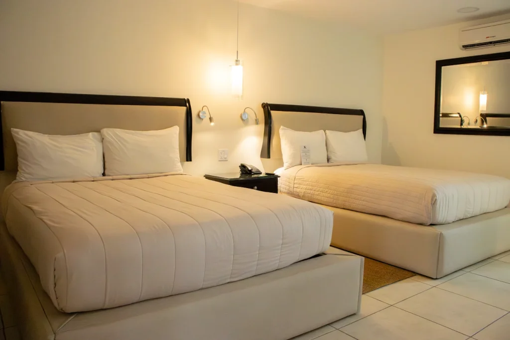 Habitaci&oacute;n de hotel con dos camas y cabeceras negras, luz tenue y espejo.