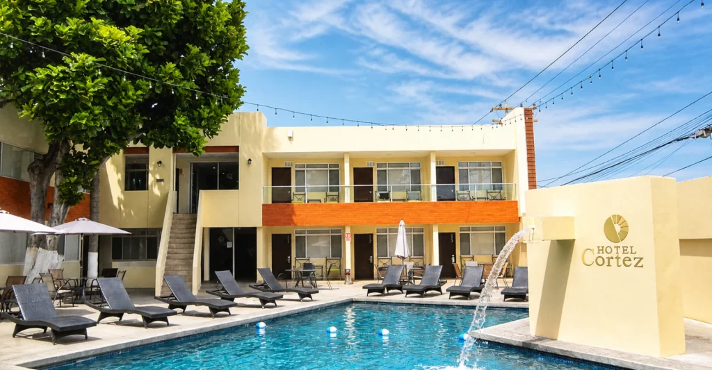 Piscina y terraza con camastros, toldos y fachada del Hotel Cortez