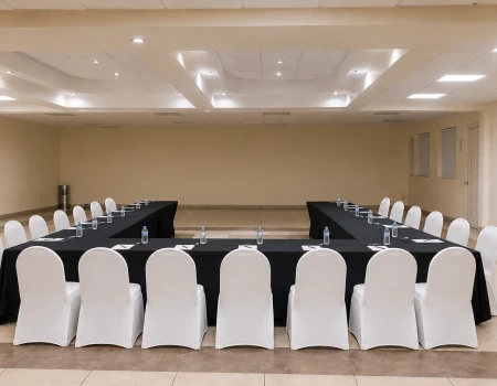 Sala de reuniones con mesas, sillas blancas y mesas de servicio para eventos
