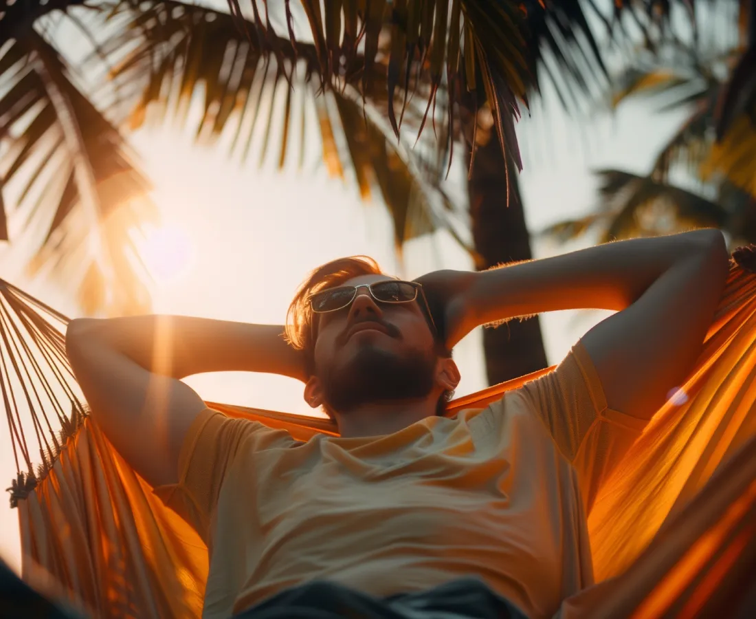 Hombre en hamaca, con sol y palmeras al atardecer, mirando al cielo