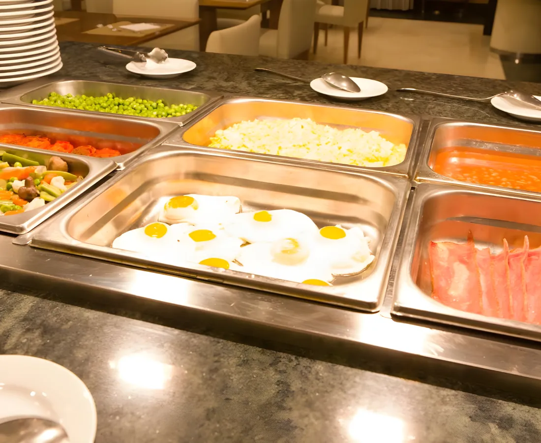 Mesa de buffet con huevos fritos, verduras y pescado en recipientes met&aacute;licos