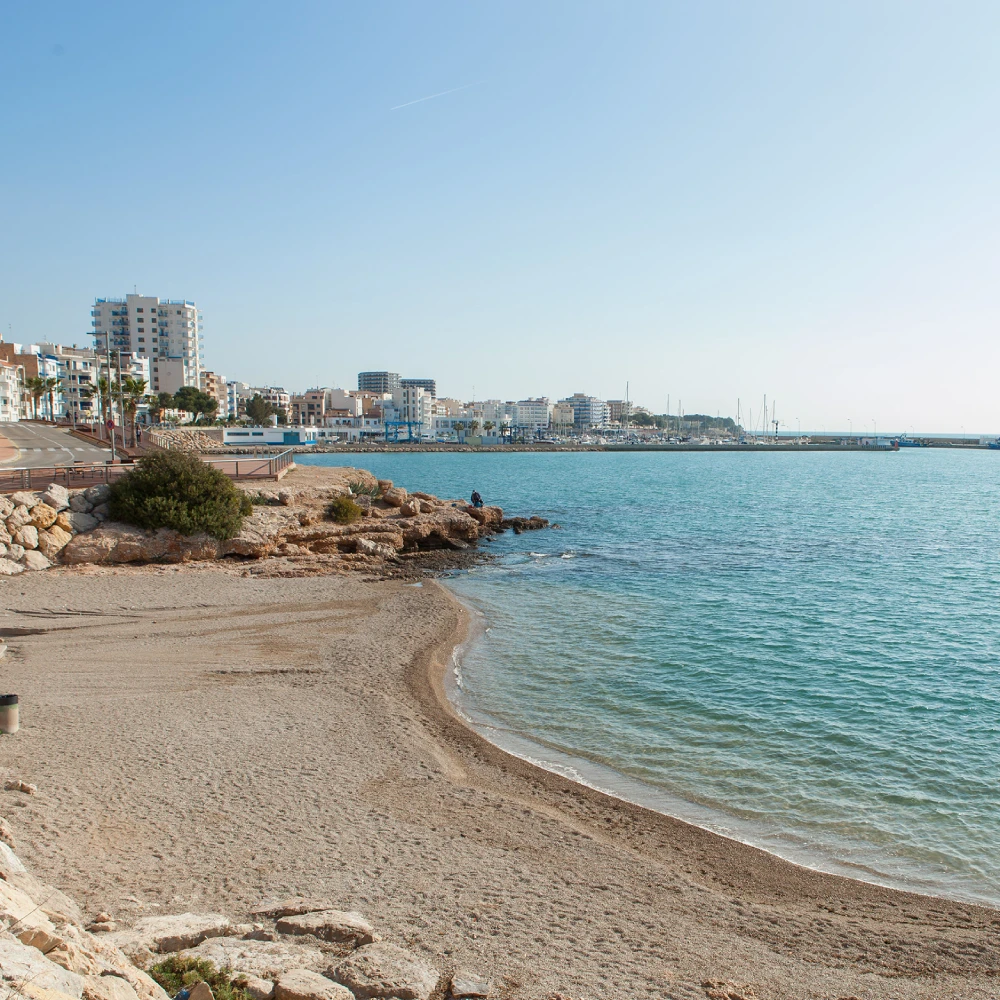 Costa con paseo y edificios junto al mar, cielo despejado y olas suaves.