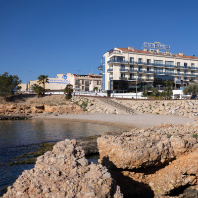 Hotel junto al mar con cielo azul y rocas en la orilla.