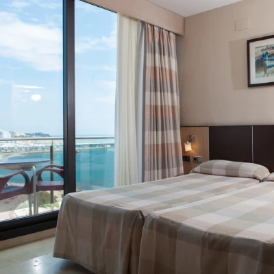 Habitaci&oacute;n de hotel con cama y balc&oacute;n frente al mar, con cortinas.