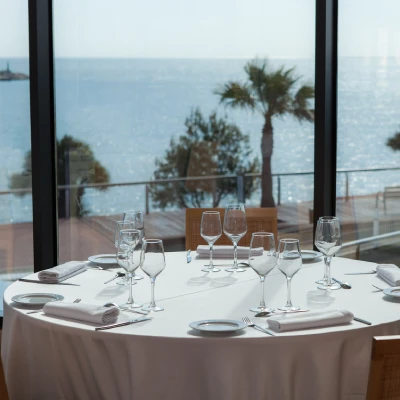 Mesa puesta para cena con copas y vistas al mar desde un ventanal