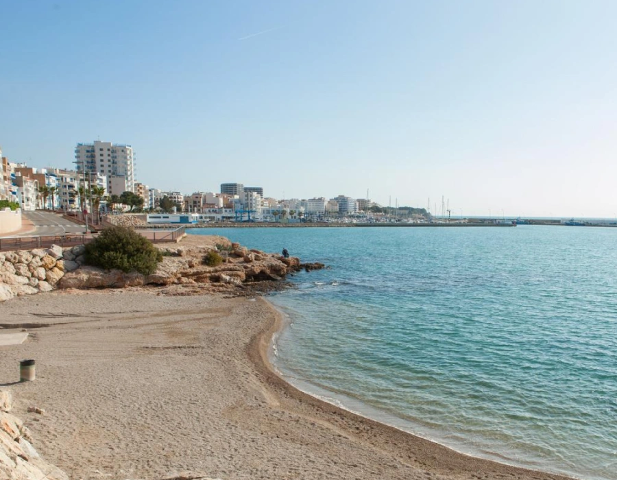 Playa con costa rocosa y edificios junto al mar, cielo despejado
