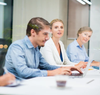 Personas en reuni&oacute;n de trabajo, una mujer habla y otras colaboran con PC.