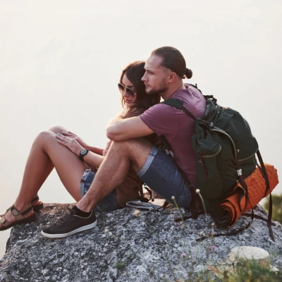 Pareja turista abrazada, con mochila y descansando sobre una roca