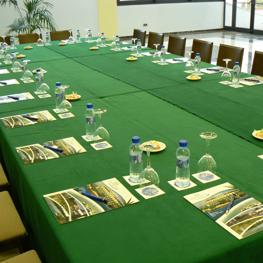 Mesa de banquete con manteler&iacute;a verde, botellas, copas y material de presentaci&oacute;n