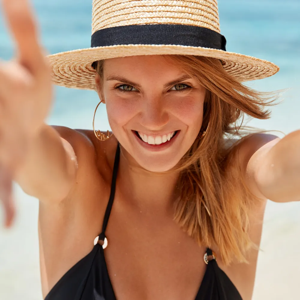 Mujer sonriente con sombrero de paja y bikini negro en la playa