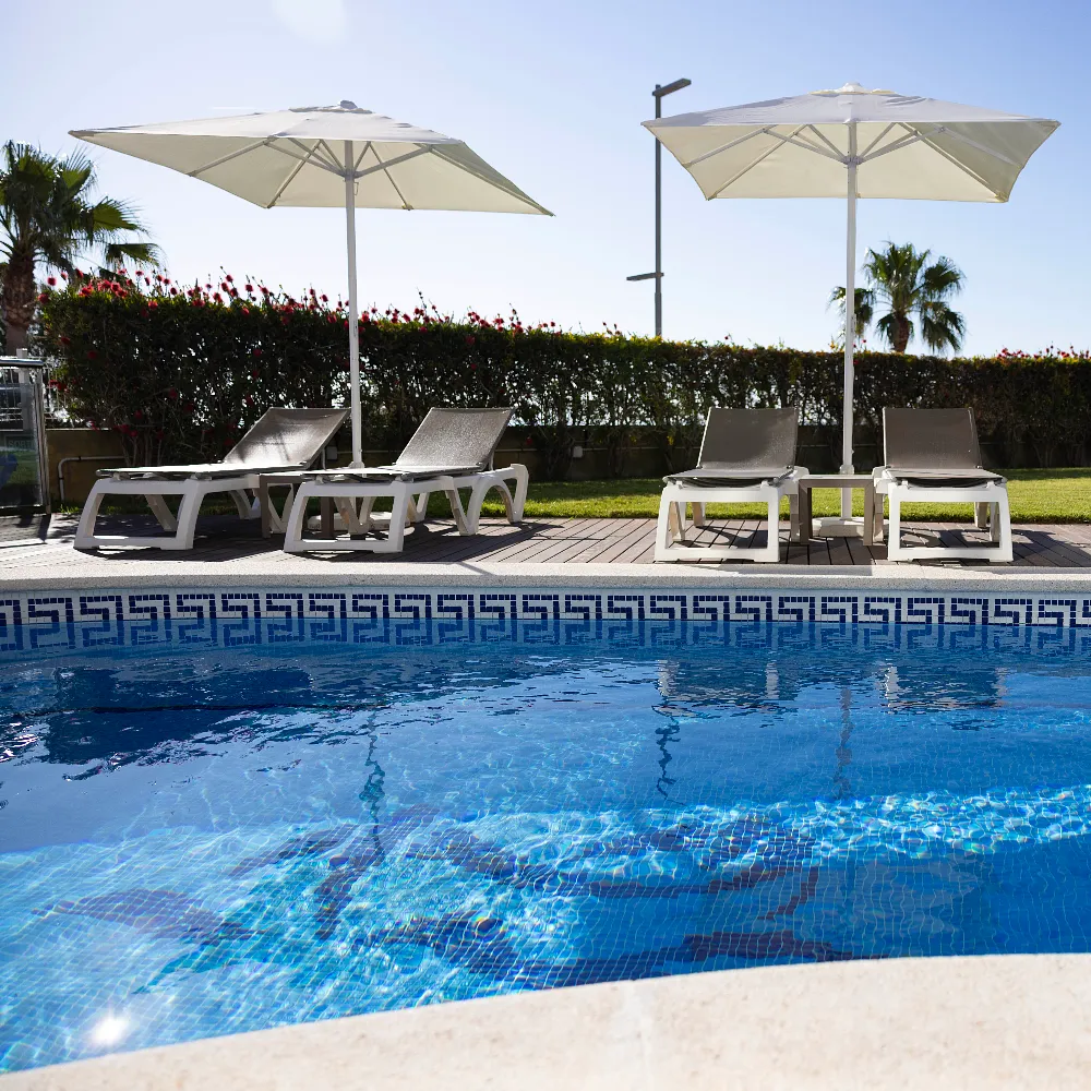 Piscina con tumbonas y sombrillas beige, jard&iacute;n y setos al fondo