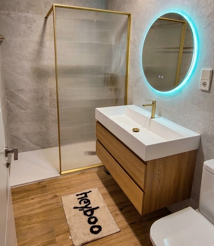 Baño moderno con lavabo de madera, espejo LED y mampara de vidrio.