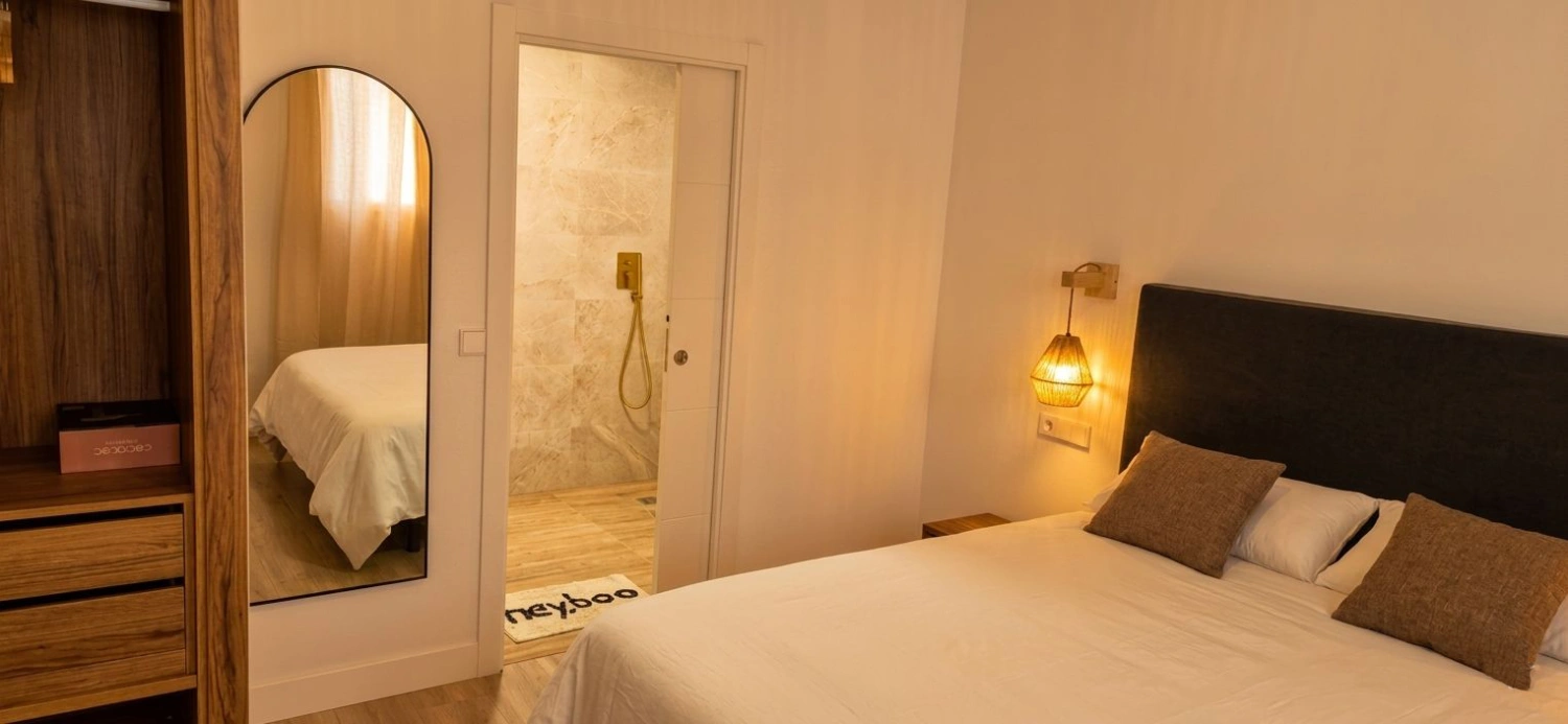 Habitación de hotel con cama doble, lámpara de pared y espejo grande.