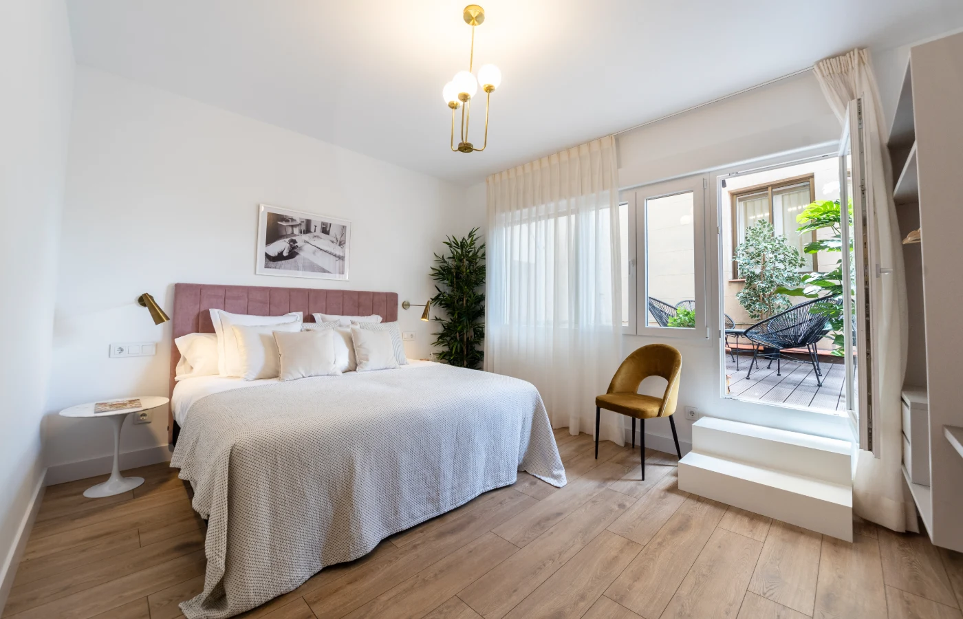 Dormitorio moderno con cama, cortinas blancas y acceso a balc&oacute;n con plantas