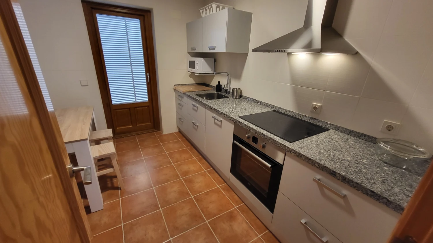 Cocina moderna con encimera de granito, vitrocerámica y horno; suelo de azulejos
