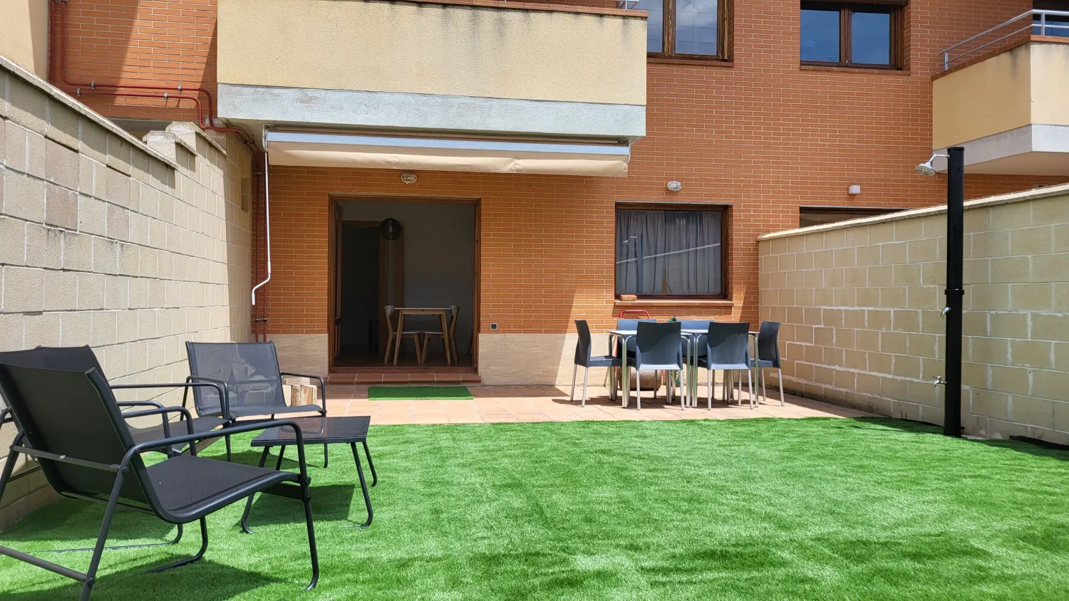 Patio con césped artificial, tumbonas y mesa con sillas en un edificio de ladrillo