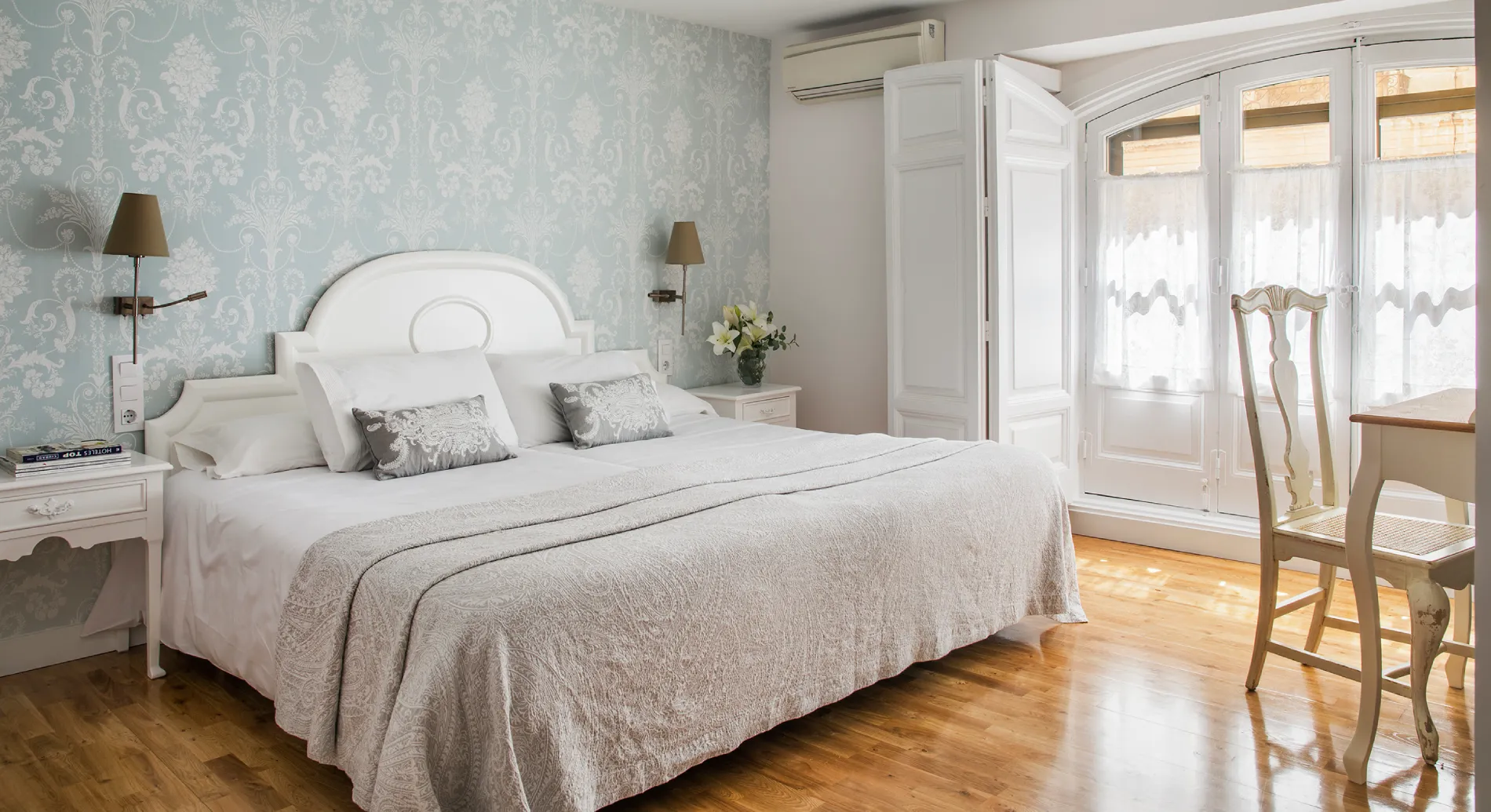 Dormitorio luminoso con cama blanca, papel tapiz claro y armario de puertas dobles