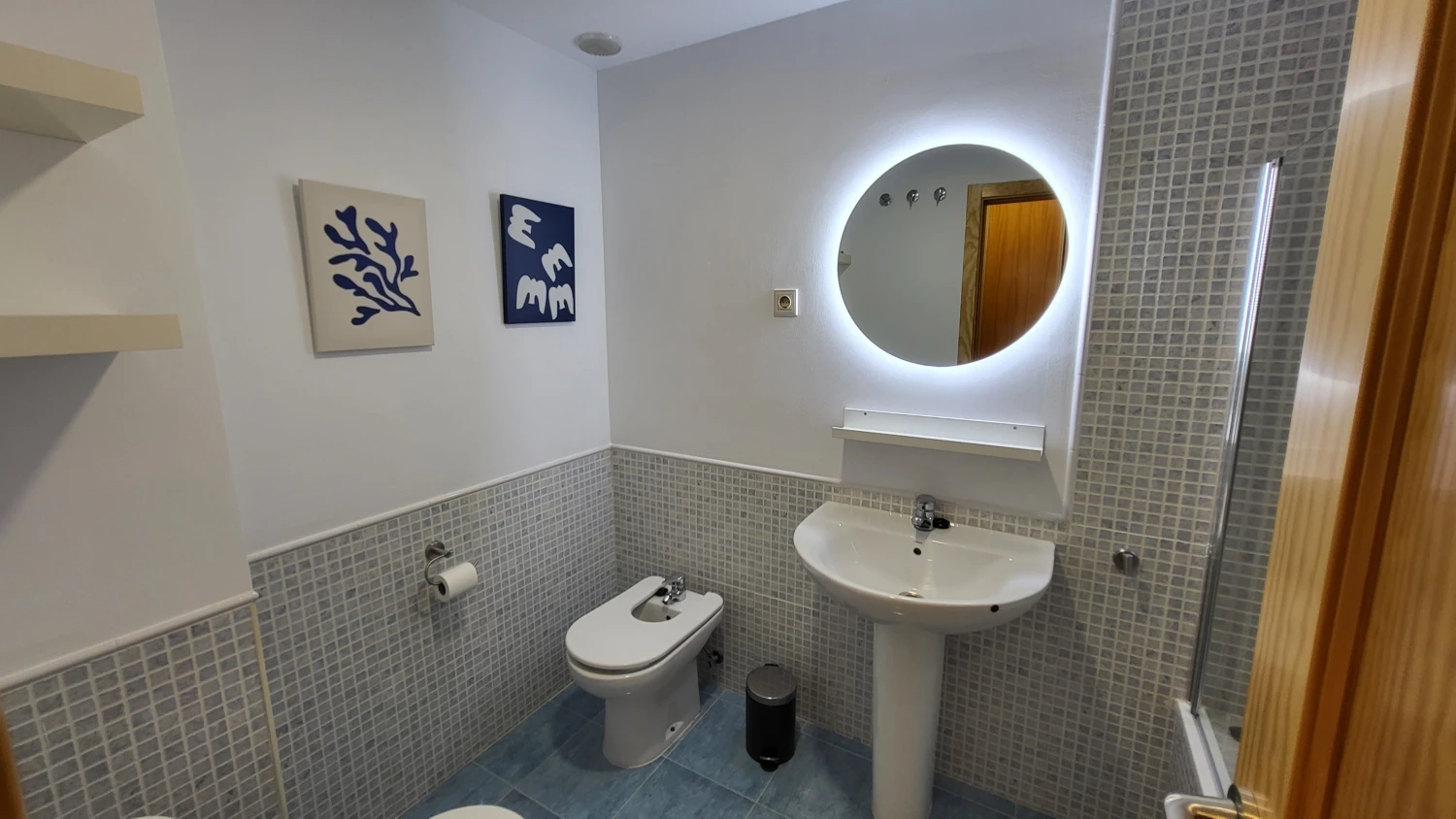 Baño moderno con lavabo, WC, ducha y espejo circular con luz LED