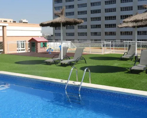 Piscina azul con tumbonas y sombrillas junto a edificio de apartamentos