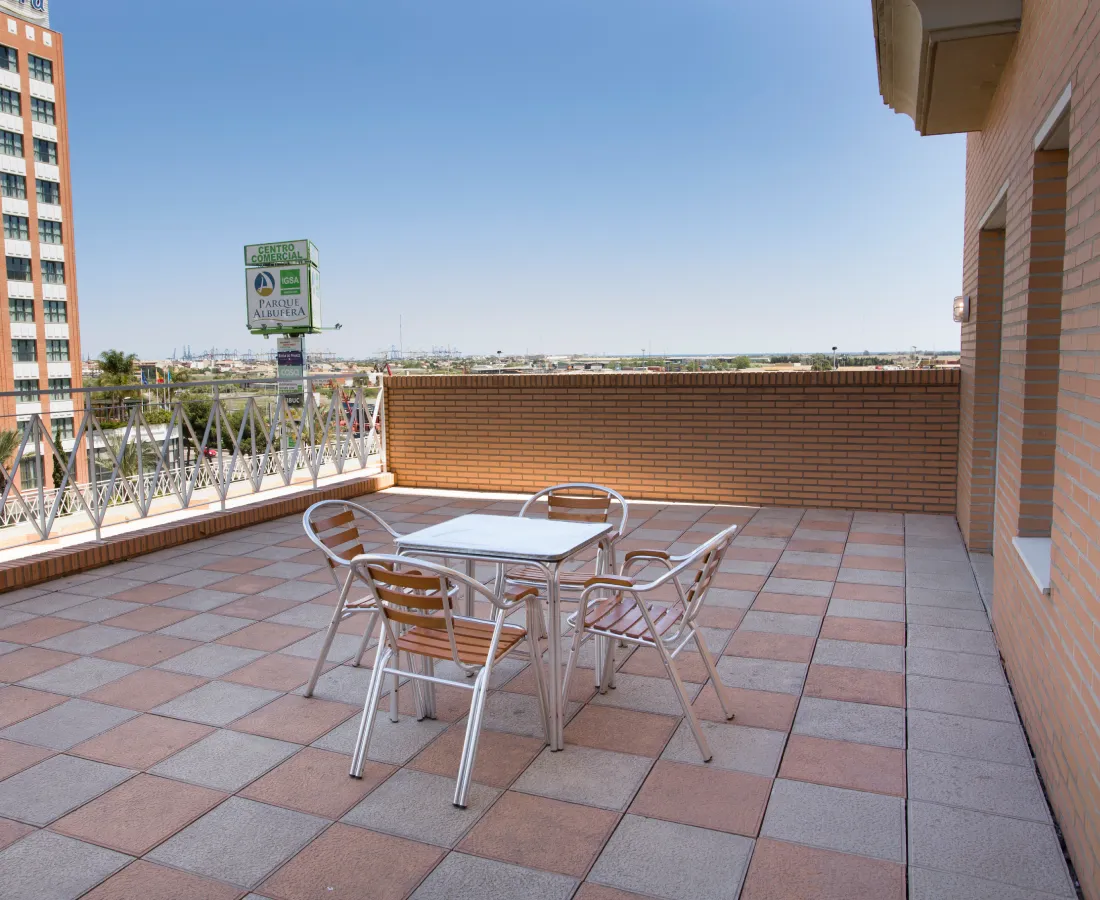 Terraza con mesa y sillas de metal, paredes de ladrillo y cielo despejado