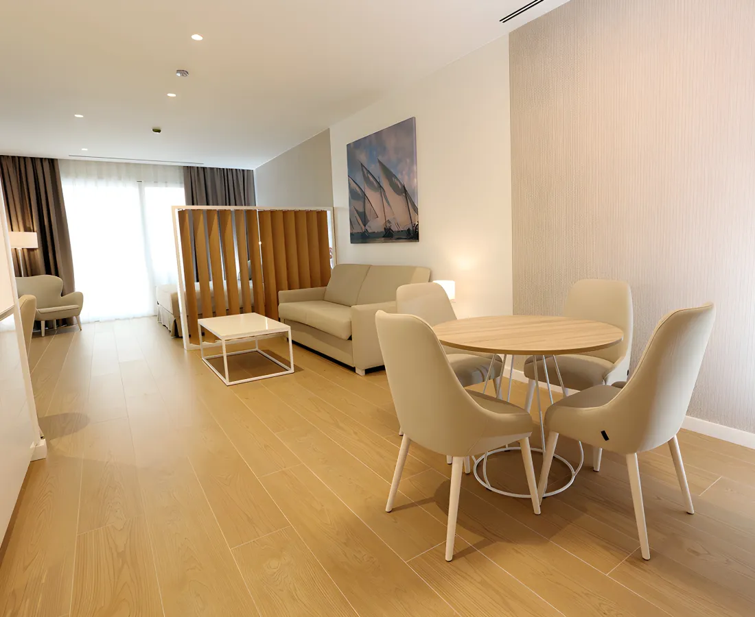 Sala moderna con mesa y sillas, sof&aacute; claro y cuadro n&aacute;utico al fondo.