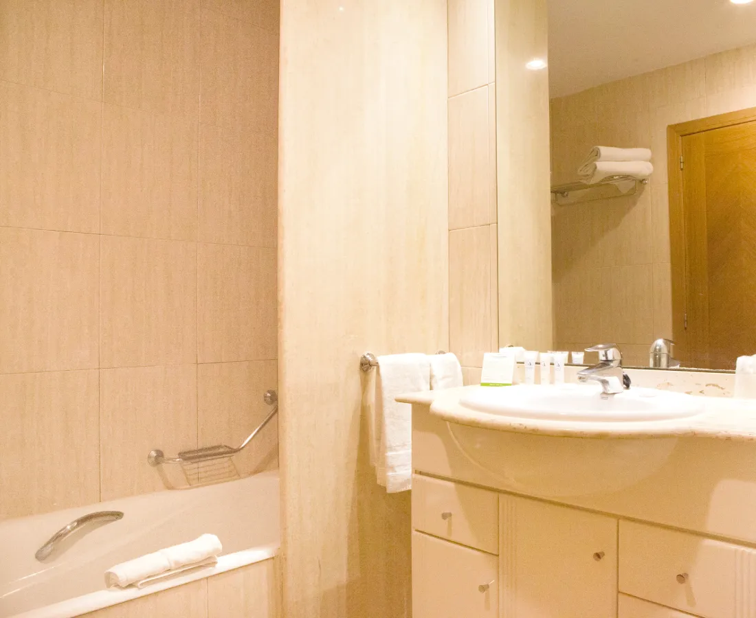 Ba&ntilde;o moderno con ba&ntilde;era, lavabo, toallas y accesorios.