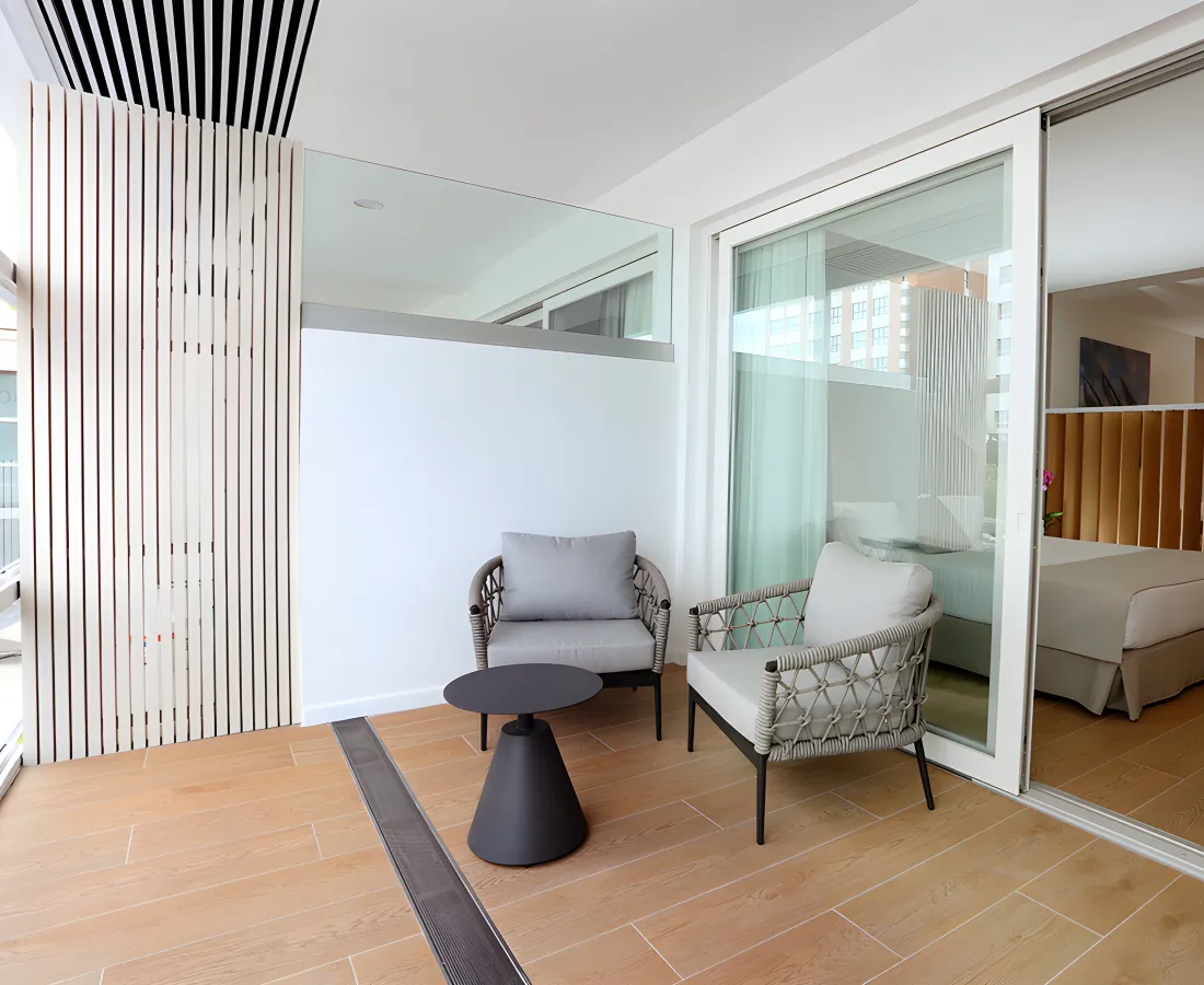 Terraza moderna con dos sillones, mesa y mamparas de vidrio en interior.