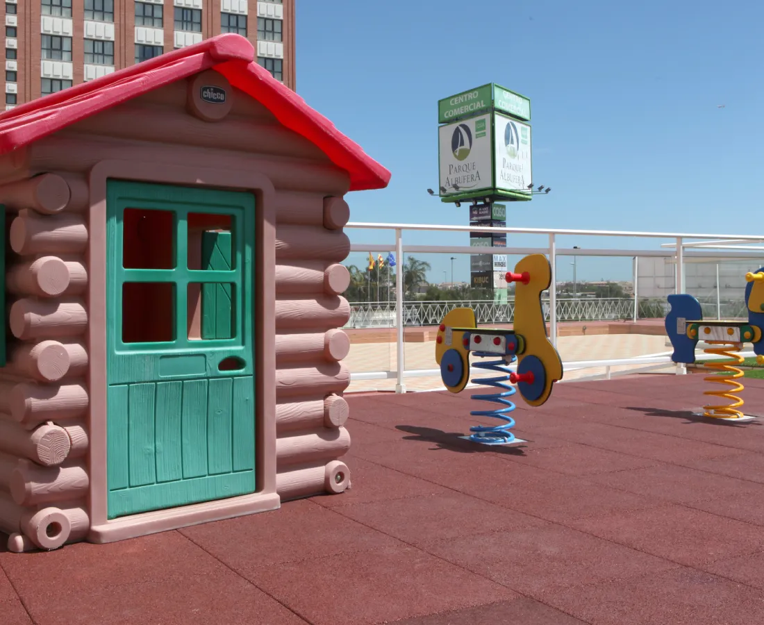 Caseta infantil de madera y juego de resorte en parque, con edificios al fondo