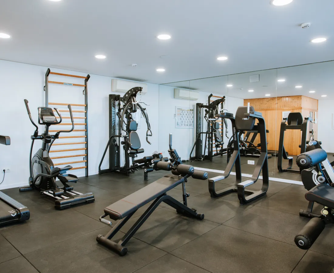 Sala de gimnasio moderna con m&aacute;quinas de cardio y pesas, en interior luminoso.