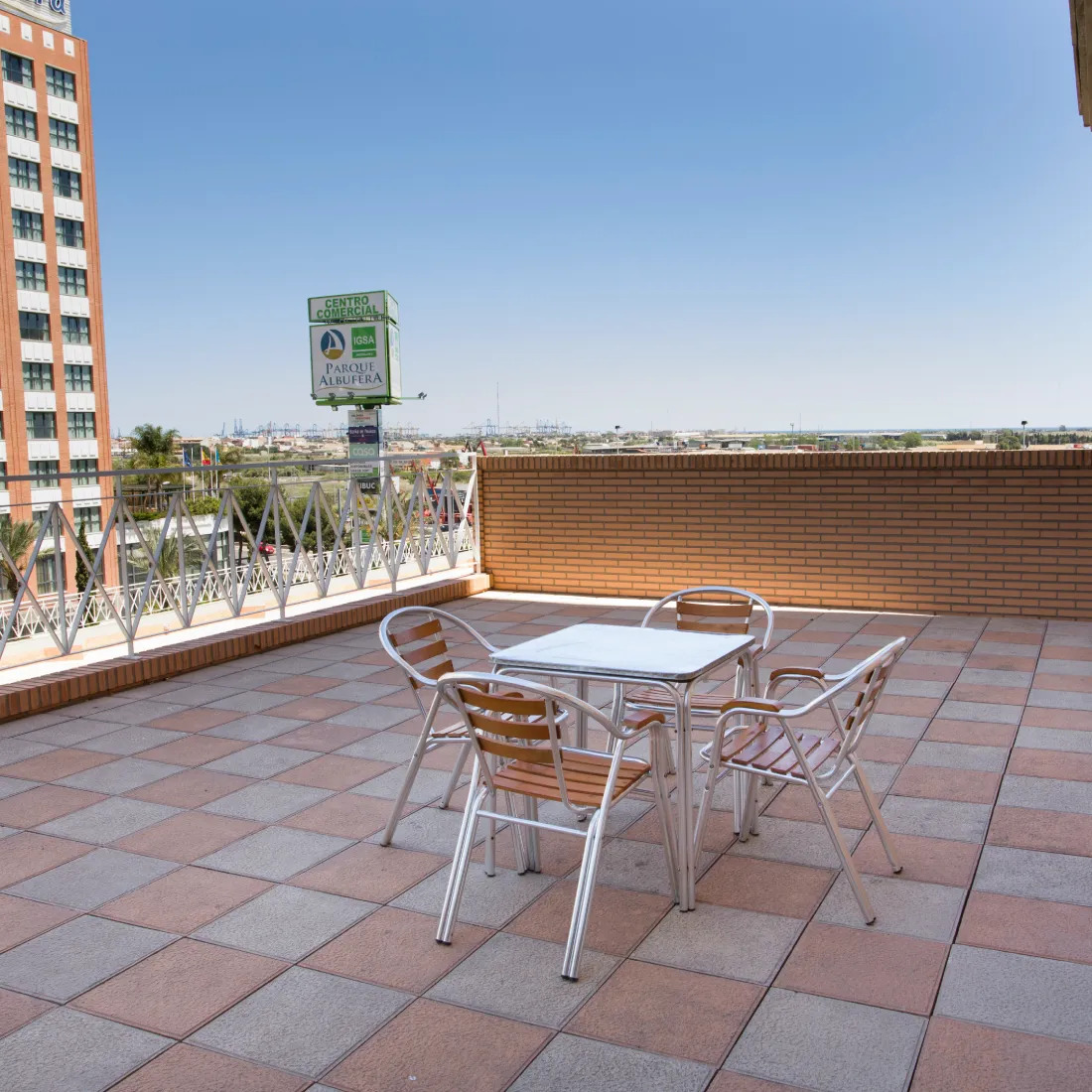Terraza con mesa y sillas de metal; vista al paisaje y letrero comercial.