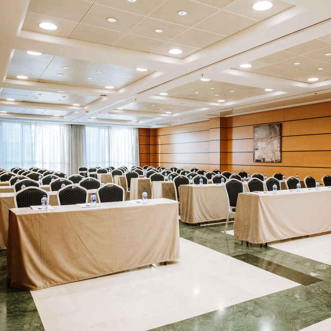 Sala de conferencias con filas de sillas y mesas, luz de techo y cortinas