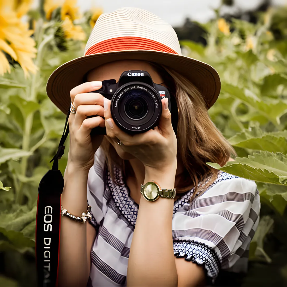 Mujer con sombrero y c&aacute;mara Canon fotografiando entre hojas verdes