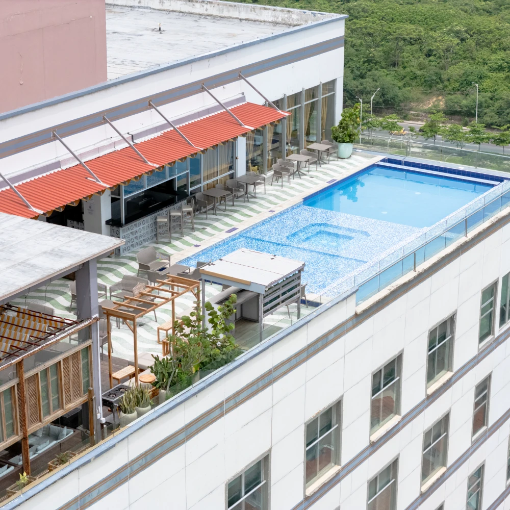 Terraza de hotel con piscina, mesas y sombrillas rojas, vista al jard&iacute;n
