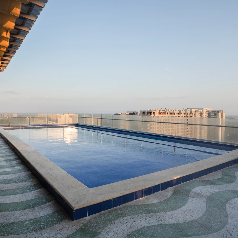 Piscina en azotea con vista al mar y edificios al atardecer