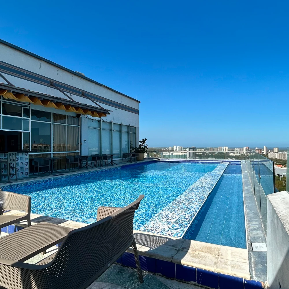 Piscina al aire libre con sillas y vista urbana bajo cielo azul