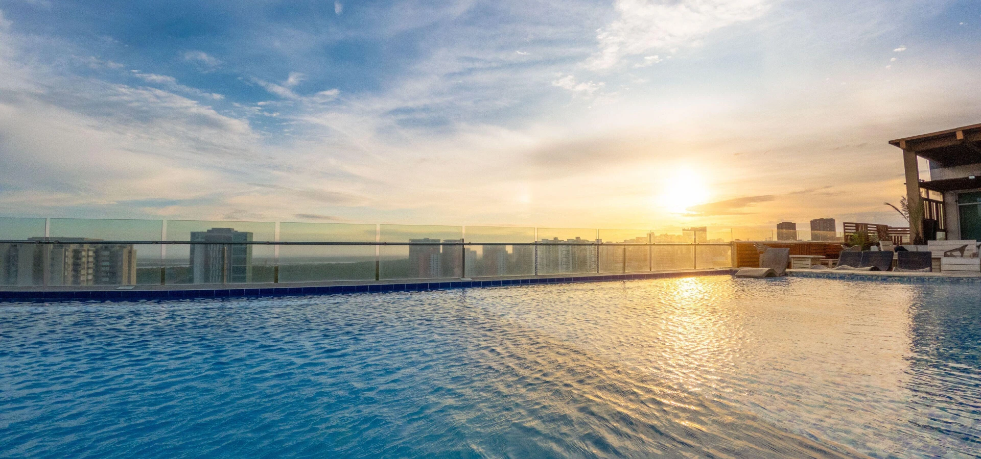 Piscina en azotea con vista urbana al atardecer y el sol sobre el horizonte