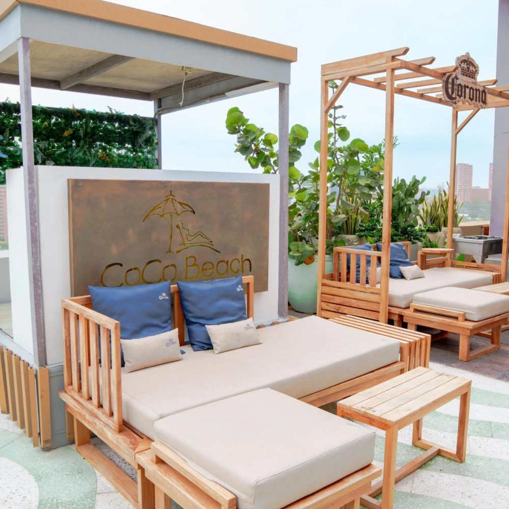 Terraza con camas de madera y cojines en &ldquo;CoCo Beach&rdquo; con toldo y jard&iacute;n