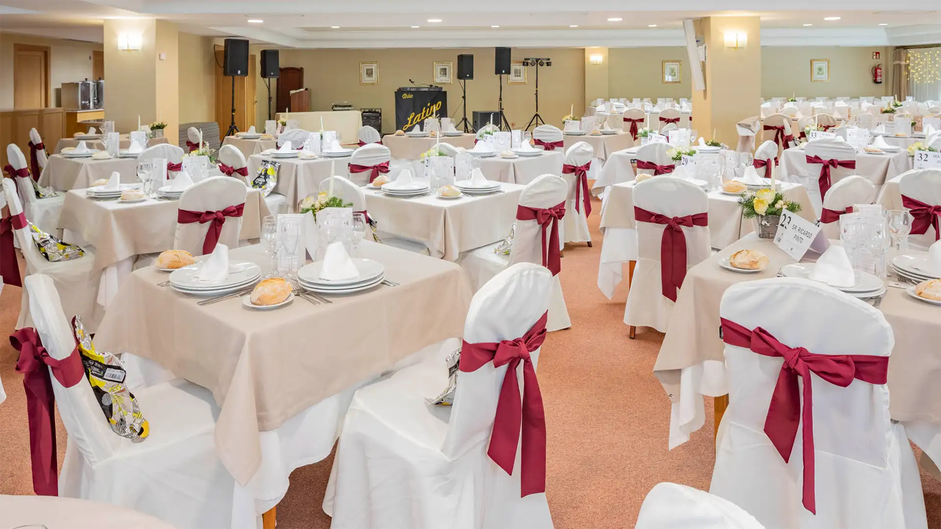Sal&oacute;n de banquete con mesas decoradas con lazos rojos y sillas cubiertas