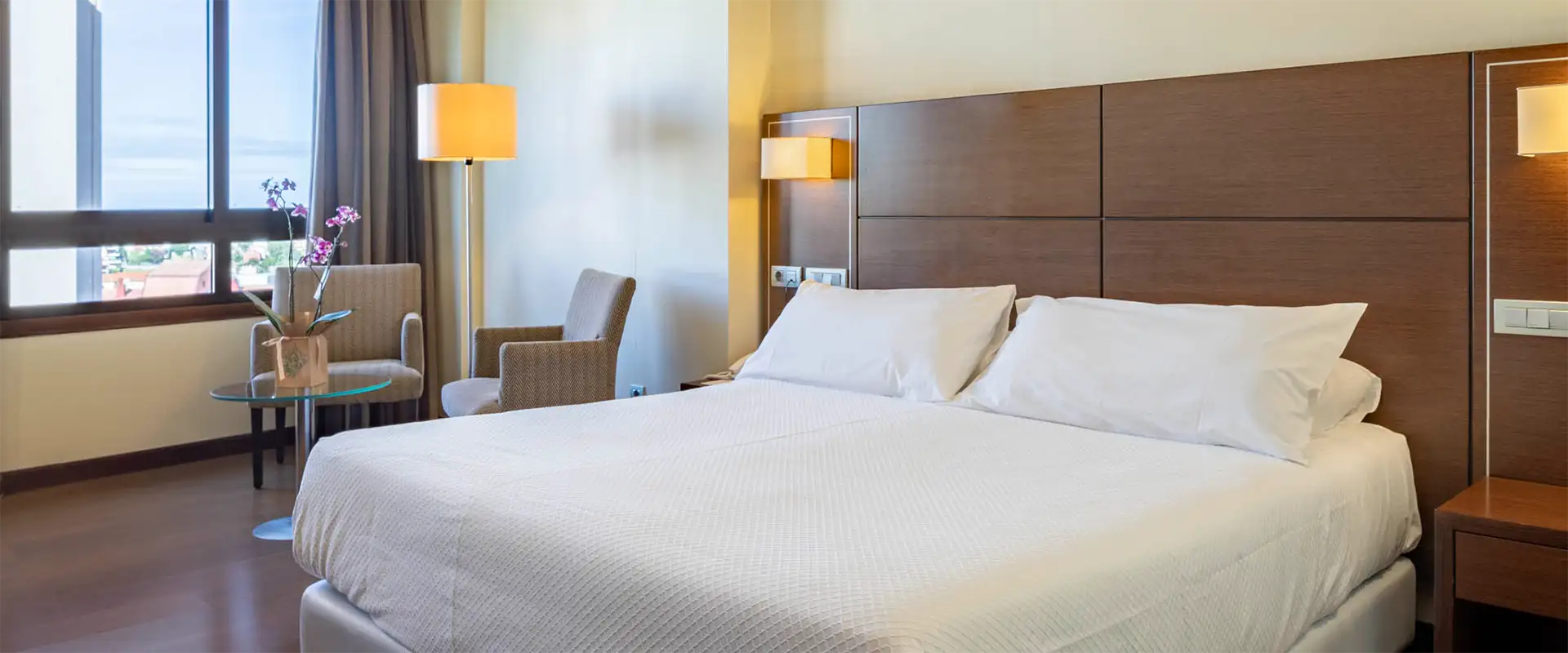 Habitaci&oacute;n de hotel con cama doble y l&aacute;mparas de pared, vista a ventanas
