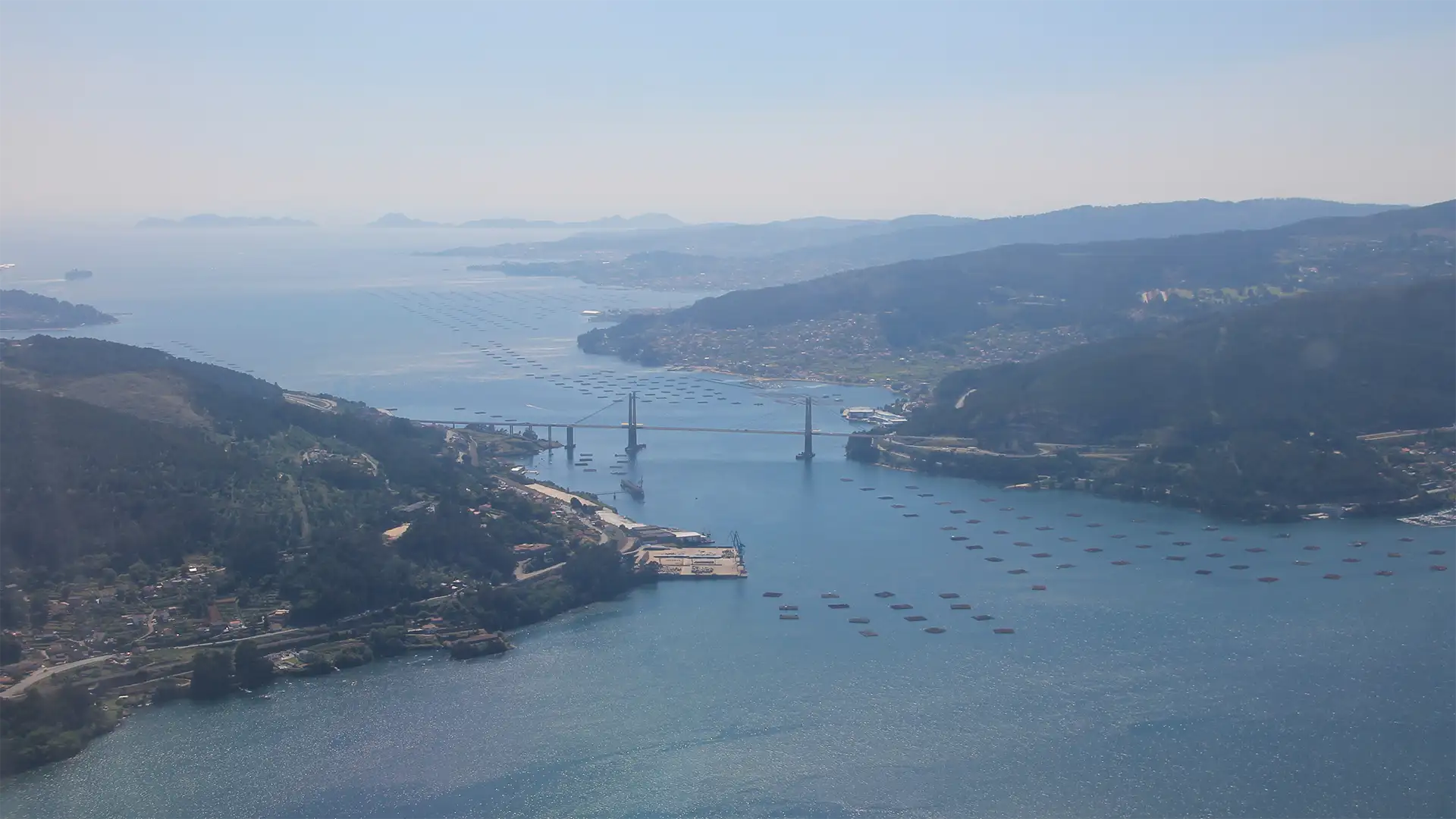 Bah&iacute;a con barcazas amarradas y puente sobre un r&iacute;o entre monta&ntilde;as, al atardecer