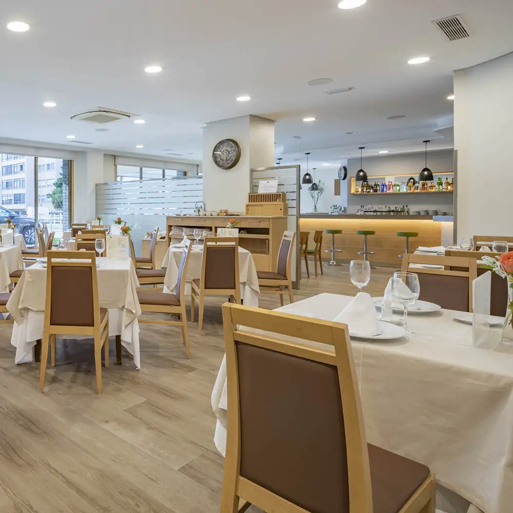Comedor de restaurante con mesas, sillas y barra de bar al fondo