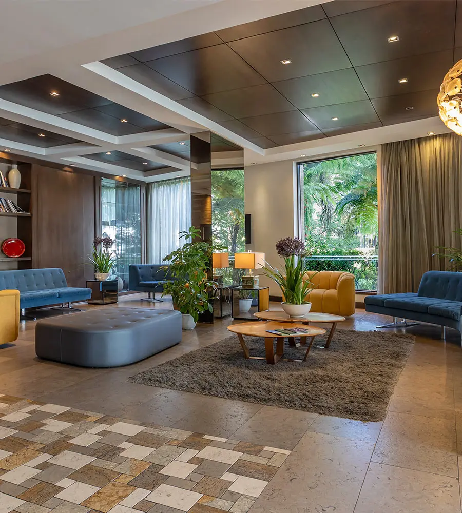 Sala moderna con sof&aacute;s azules, sillones amarillos, plantas y ventanales al jard&iacute;n