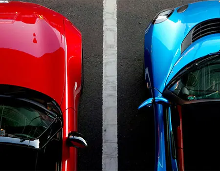 Dos autos, uno rojo y otro azul, separados por una l&iacute;nea blanca en asfalto.
