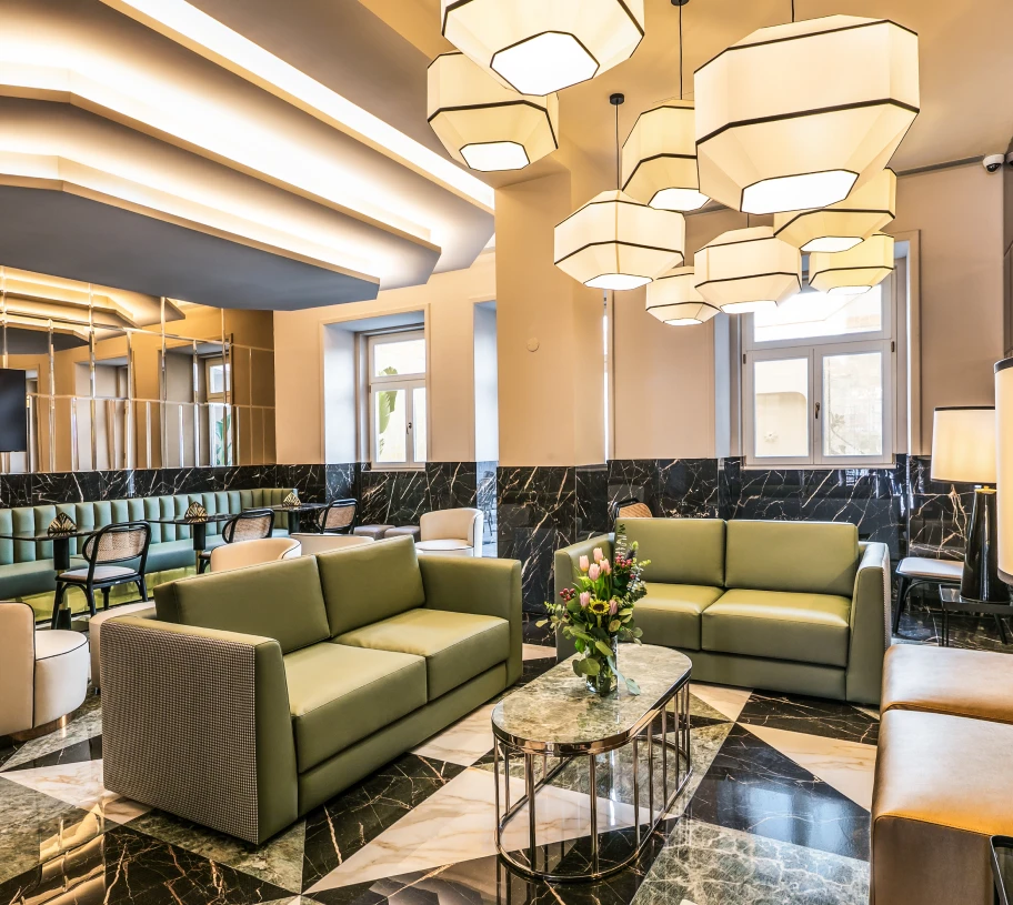 Sala moderna com sof&aacute;s verdes, mesa de m&aacute;rmore e lustres hexagonais no lobby