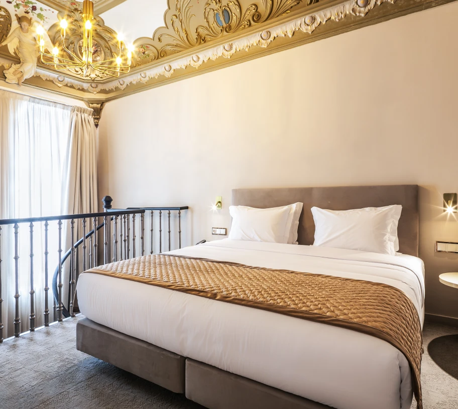 Quarto de hotel elegante com cama, lustre dourado e varanda com cortinas
